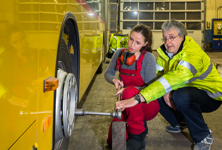 24534770 - yong woman, trainee with the master, change wheel of a buses in the work hall